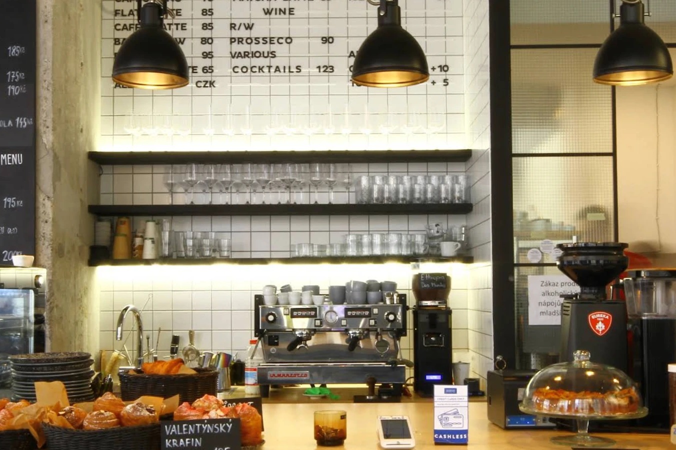 The espresso bar at Minimum Waste with a La Marzocco machine, a menu board, and a basket of pastries on the counter