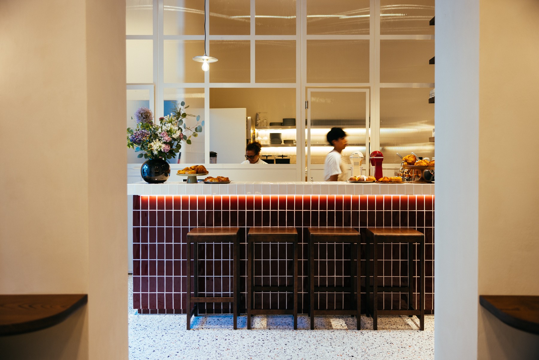 The white tiled counter and burgundy tiled bar front at Run by Nuns, bar stools lined up beneath pendant lighting