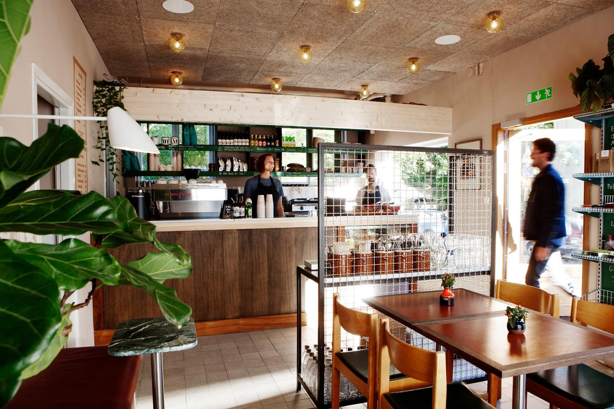 The wood panelled counter at AB Cafe in Telefonplan, with a barista behind the espresso machine and tables in the foreground