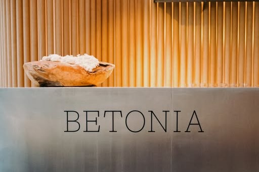The BETONIA wordmark on a steel counter in front of a curved wood slat wall inside the cafe