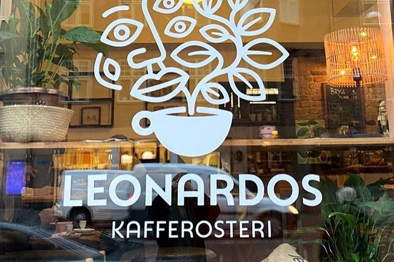 The LEONARDOS KAFFEROSTERI logo and wordmark on the arched storefront window, with plants and warm interior lighting visible behind the glass