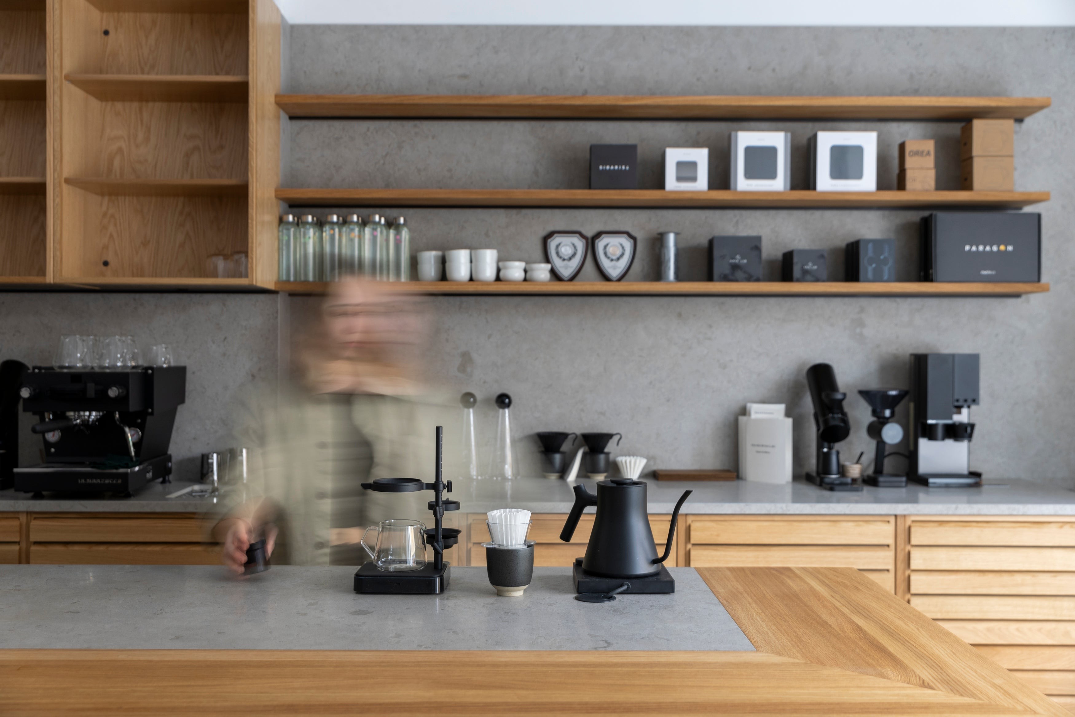The wood shelved counter at Nordic Brew Lab in Stockholm, with an espresso machine, pour over gear, and retail coffee bags on display
