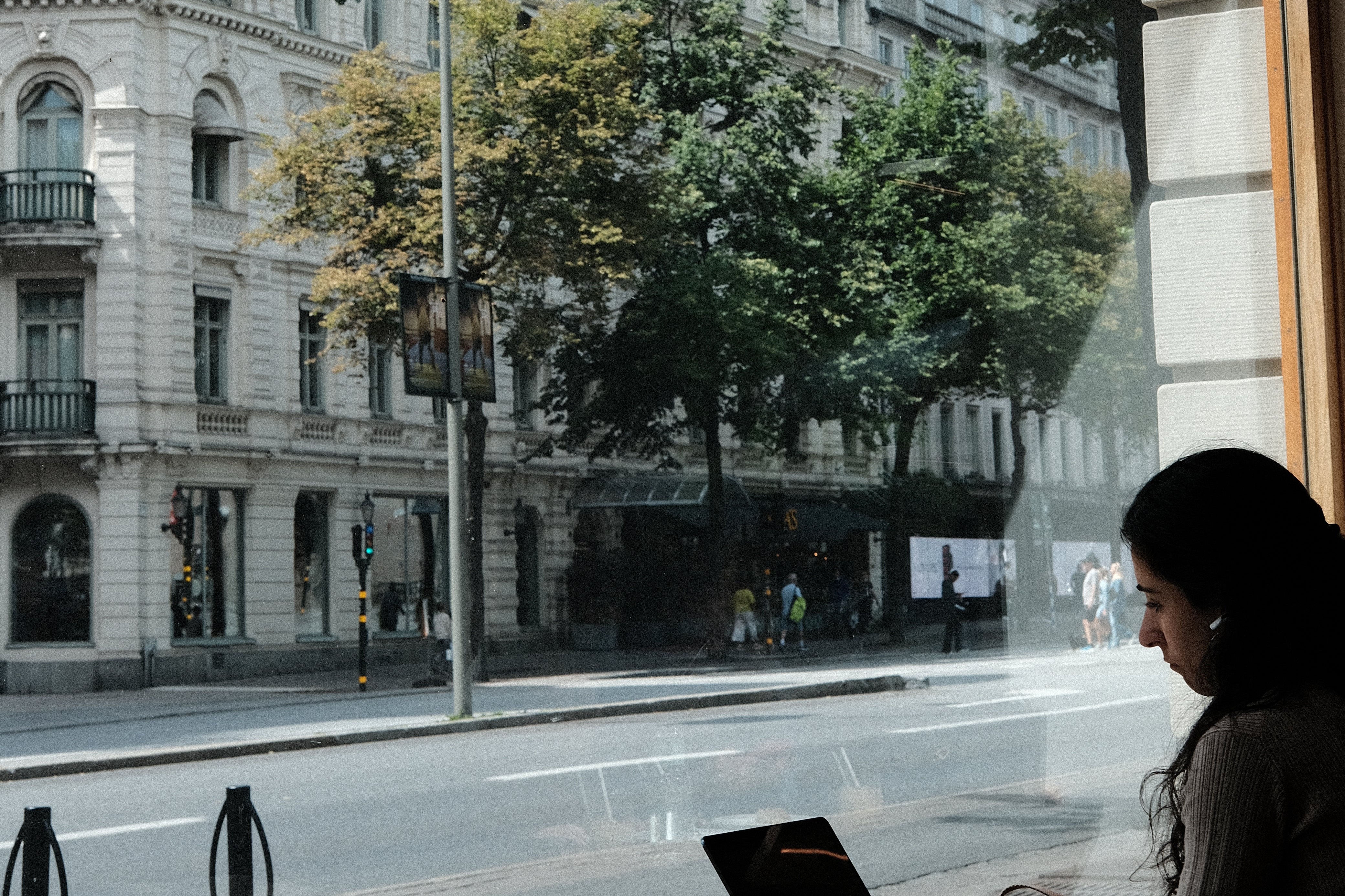 A customer working on a laptop by the window at Standout Coffee Ostermalm, with the grand facades of Ostermalm visible across the street