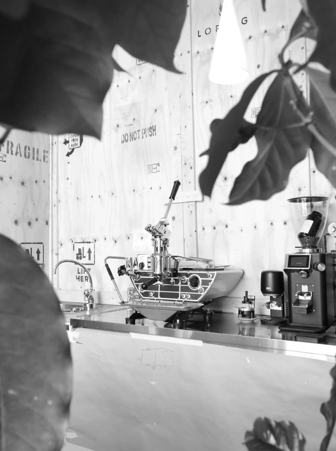 A lever espresso machine and grinder set against plywood roaster crates stamped Loring, Fragile, and Do Not Push at Standout Coffee