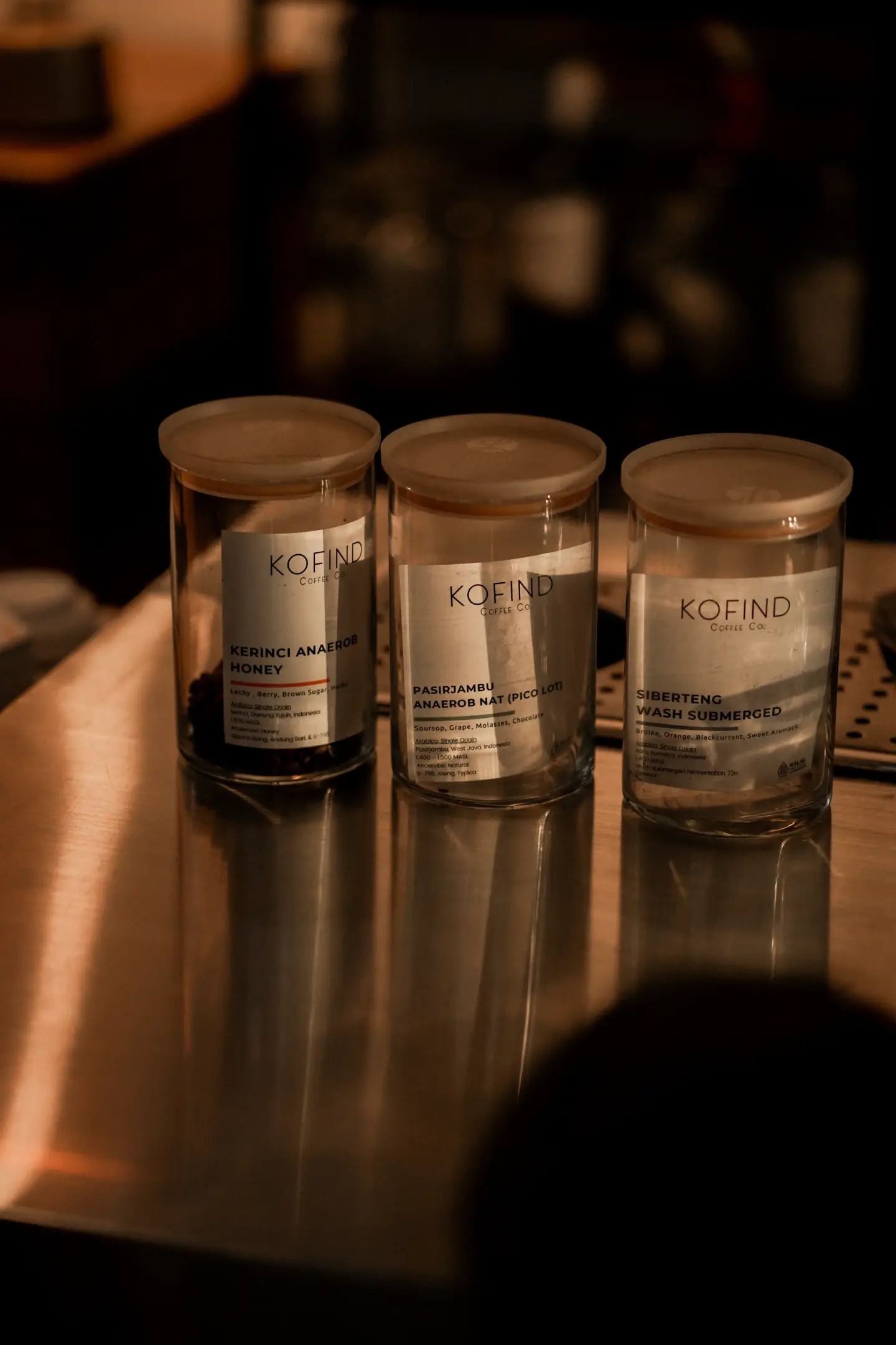 Three labeled Kofind bean jars, Kerinci Anaerob Honey, Pasirjambu Anaerob Nat and Siberteng Wash Submerged, lined up on the bar counter