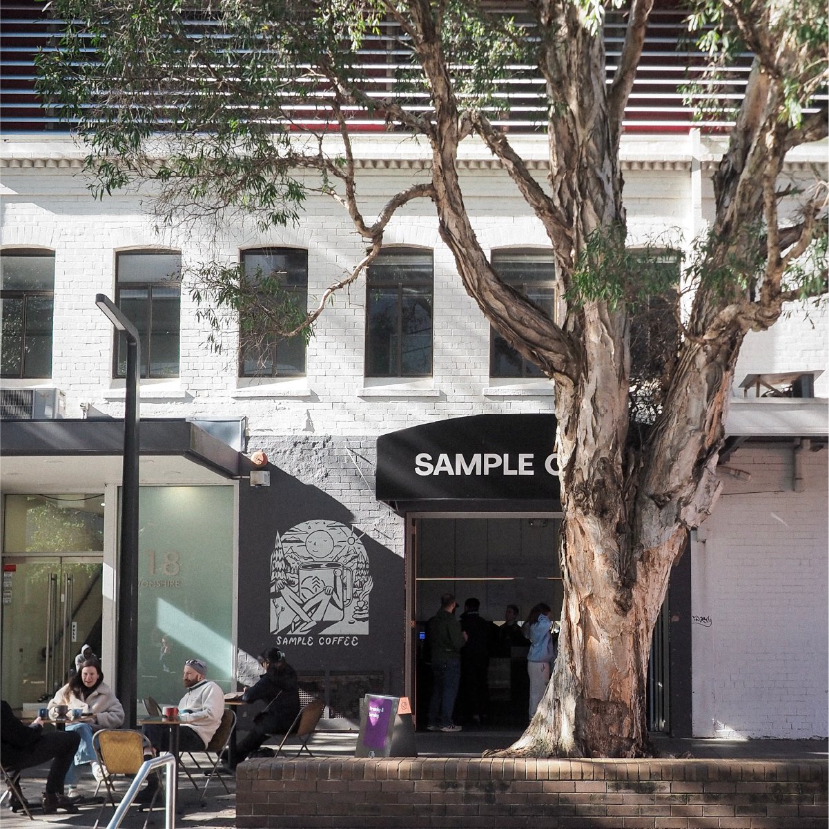 The Surry Hills storefront under a eucalyptus tree, the black awning and mural beside the entrance, a few tables out front