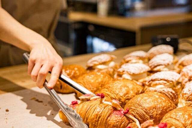 A staff member using tongs to arrange fresh croissants on the counter at Cruffin, the espresso machine visible behind