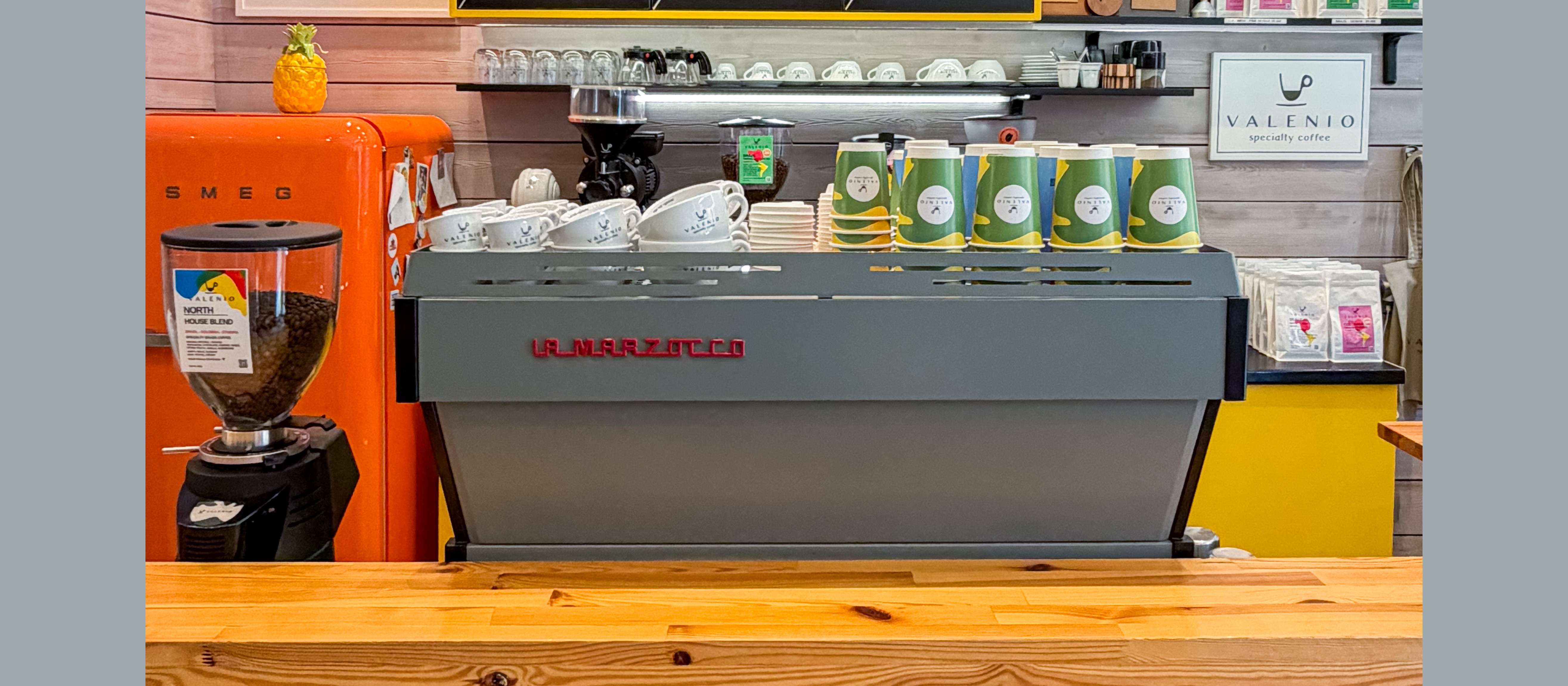 The full counter setup at Valenio, an orange Smeg fridge with a pineapple ornament, the La Marzocco machine, grinder and branded cups