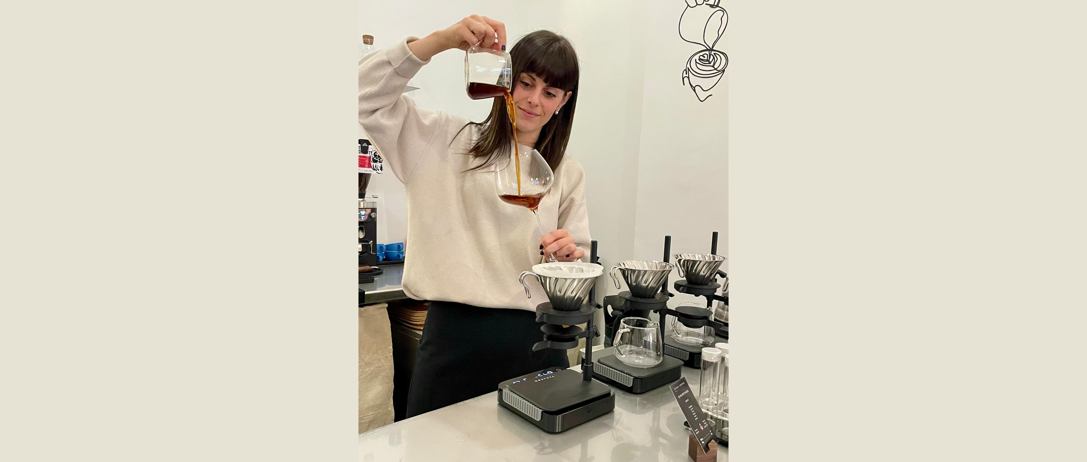 A barista at Oishii Coffee pouring a filter coffee tasting into a crystal wine glass, with pour over gear on the counter