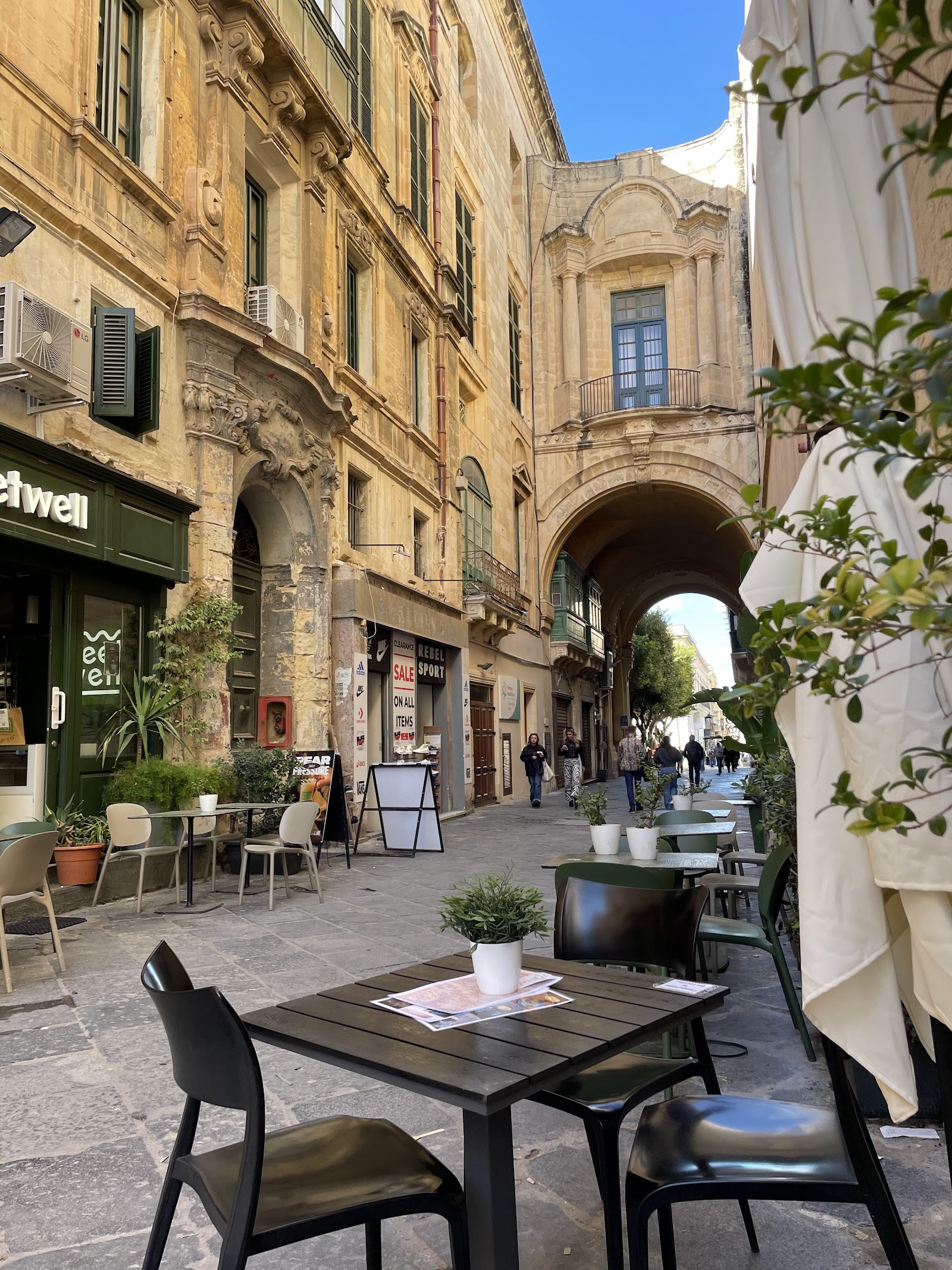 Outdoor tables under a stone archway on Old Theatre Street outside De Bono Coffee Shop
