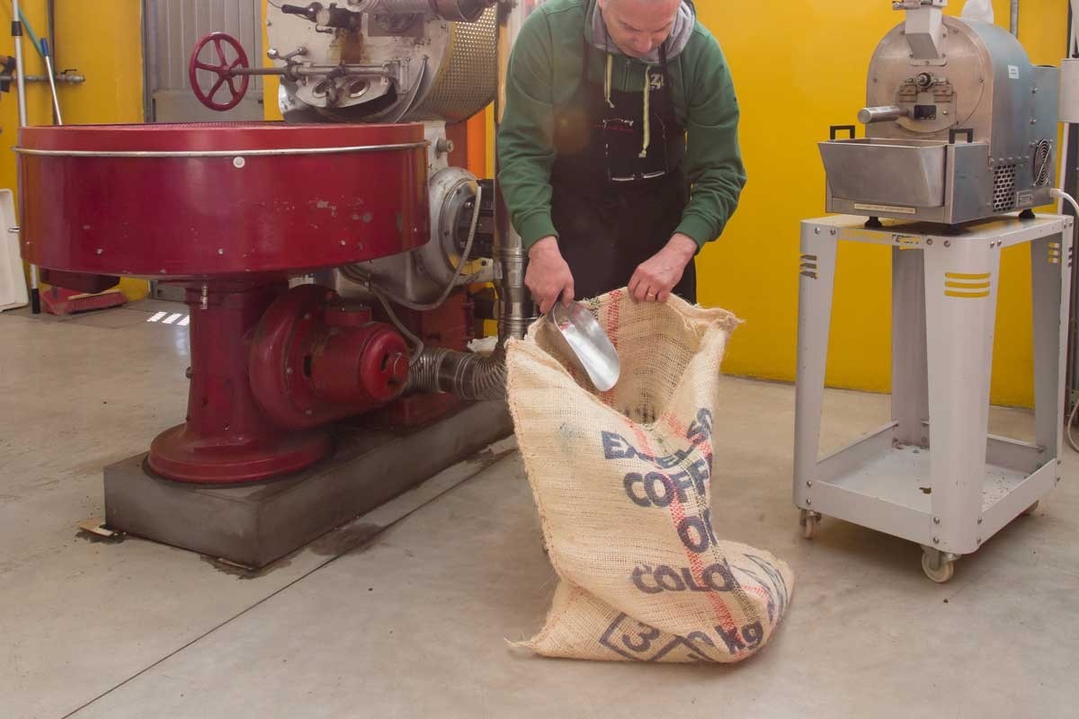 The roastery floor at Caffè Fusari, a vintage red coffee roasting machine beside a staff member scooping beans into a burlap sack