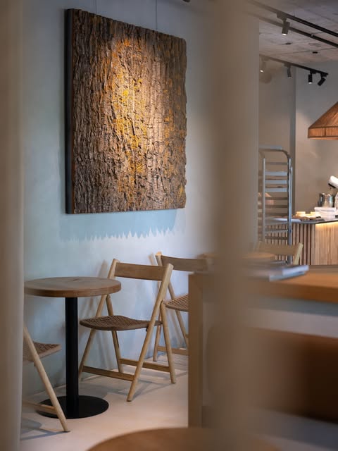 The minimal, softly lit interior of BREW Specialty Coffee with wooden folding chairs and a small round table