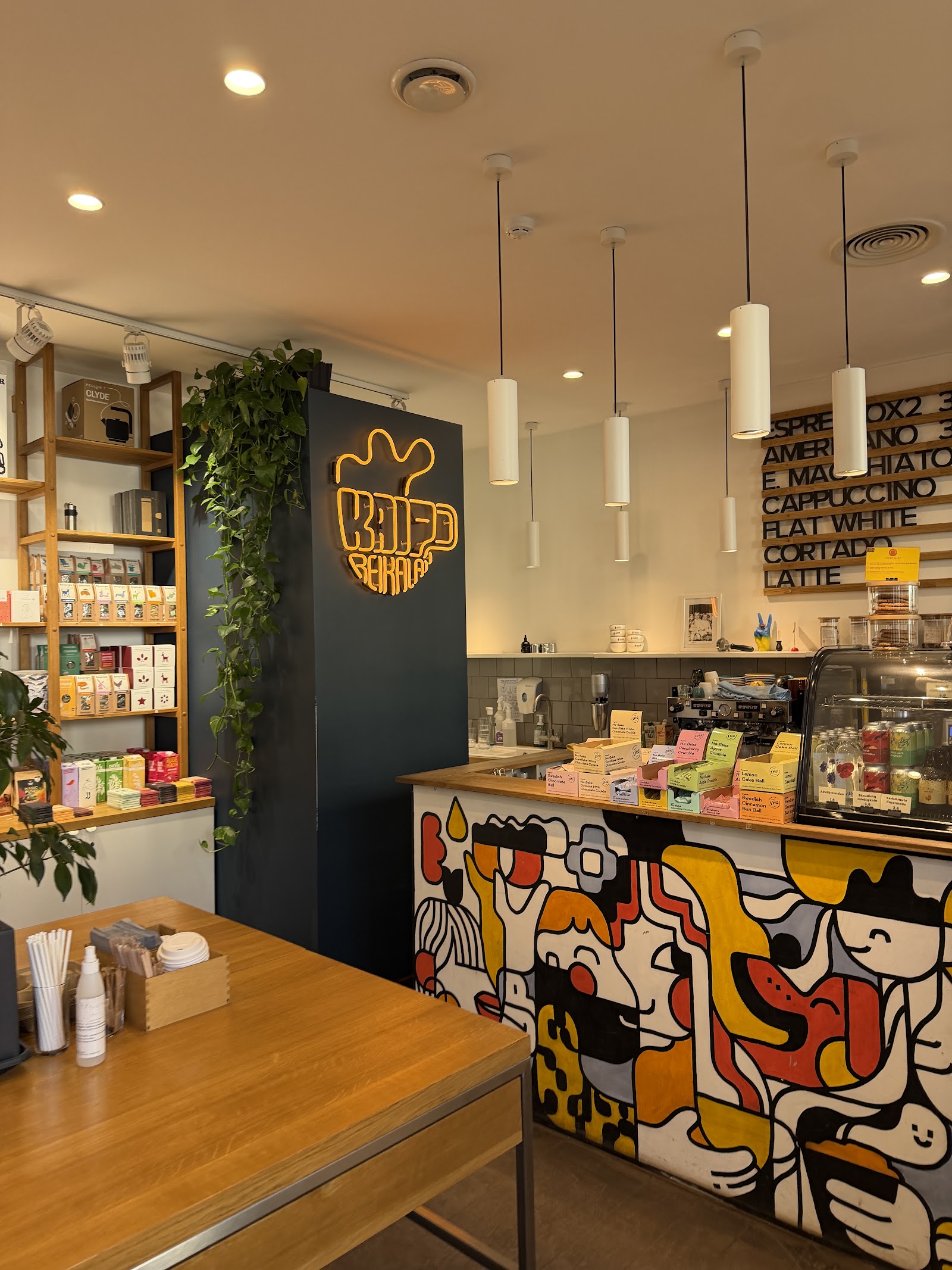The colorful mural and pendant lit interior of Kavos Reikalai with plants and cafe seating