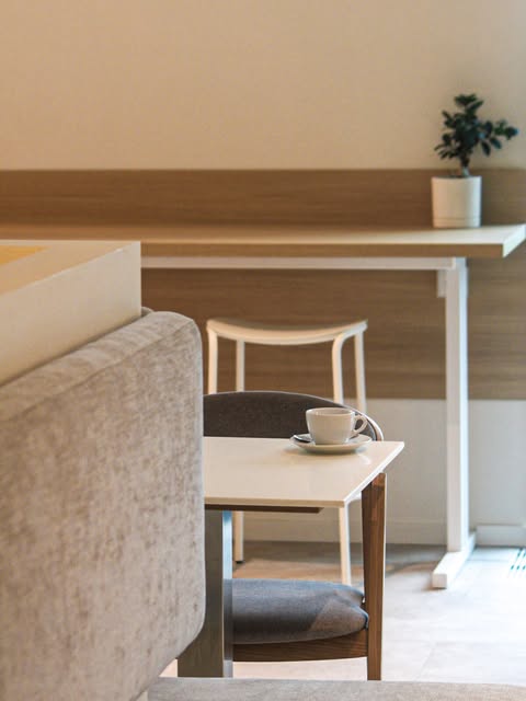 A quiet white toned corner of Strange Love Bernardinai with a small sofa, wooden desk and a cup of coffee on the table