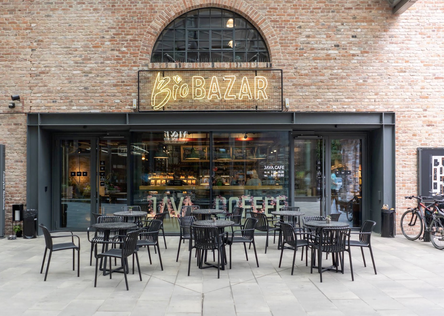 The brick exterior and glass storefront of JAVA CAFE inside Fabryka Norblina, with outdoor seating on the patio