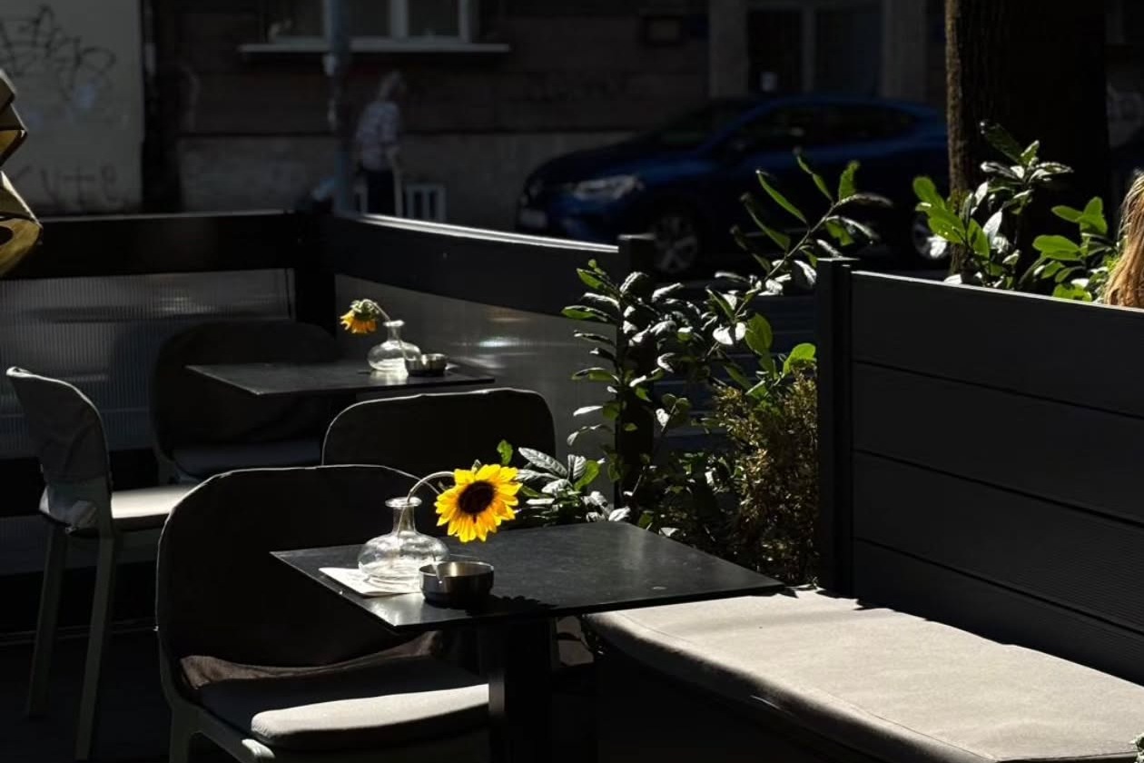 Monocycle's street terrace, black bistro tables topped with sunflowers in glass vases, greenery and the street beyond